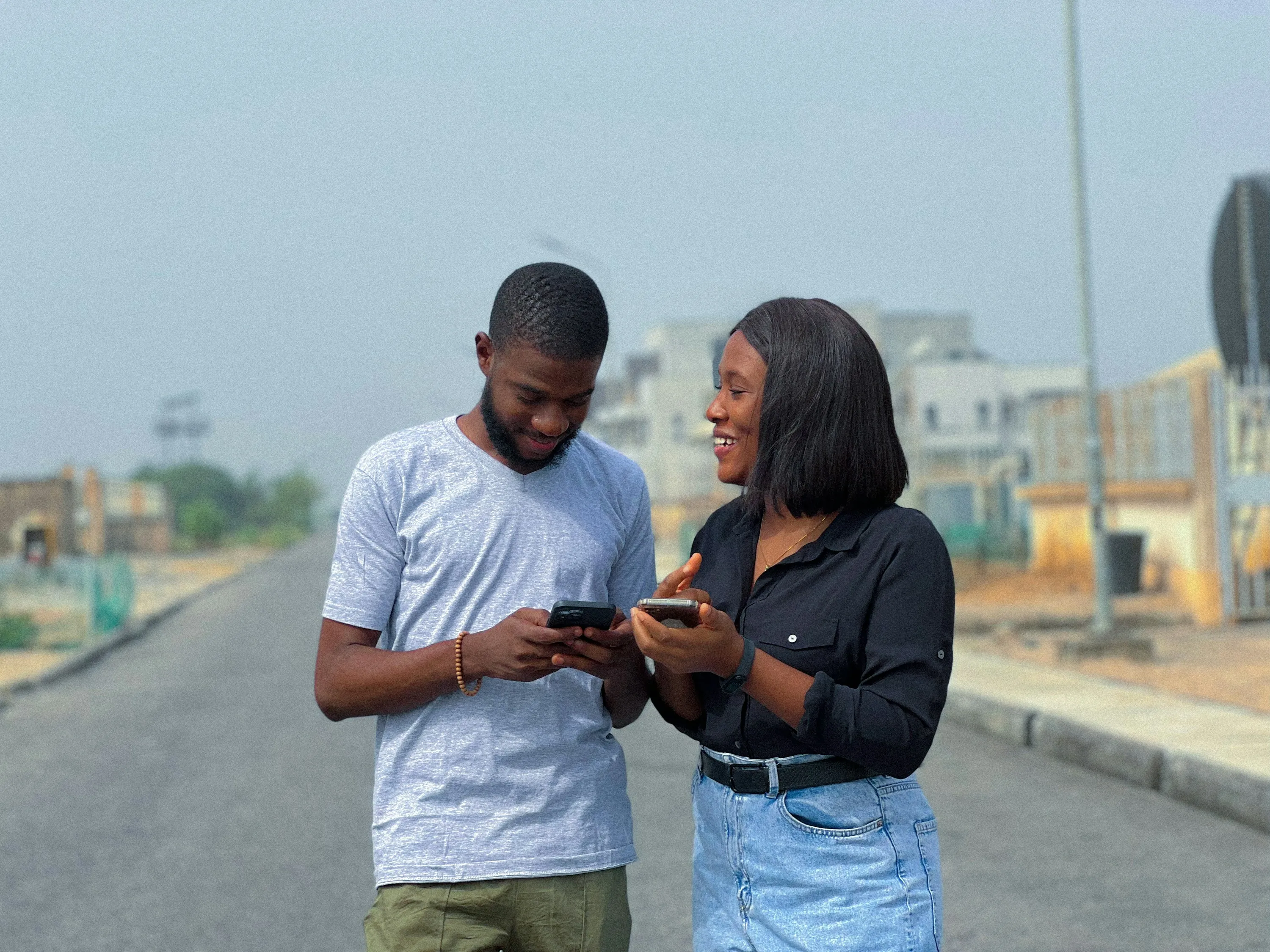 Two friends standing on a road, looking at something on a phone together